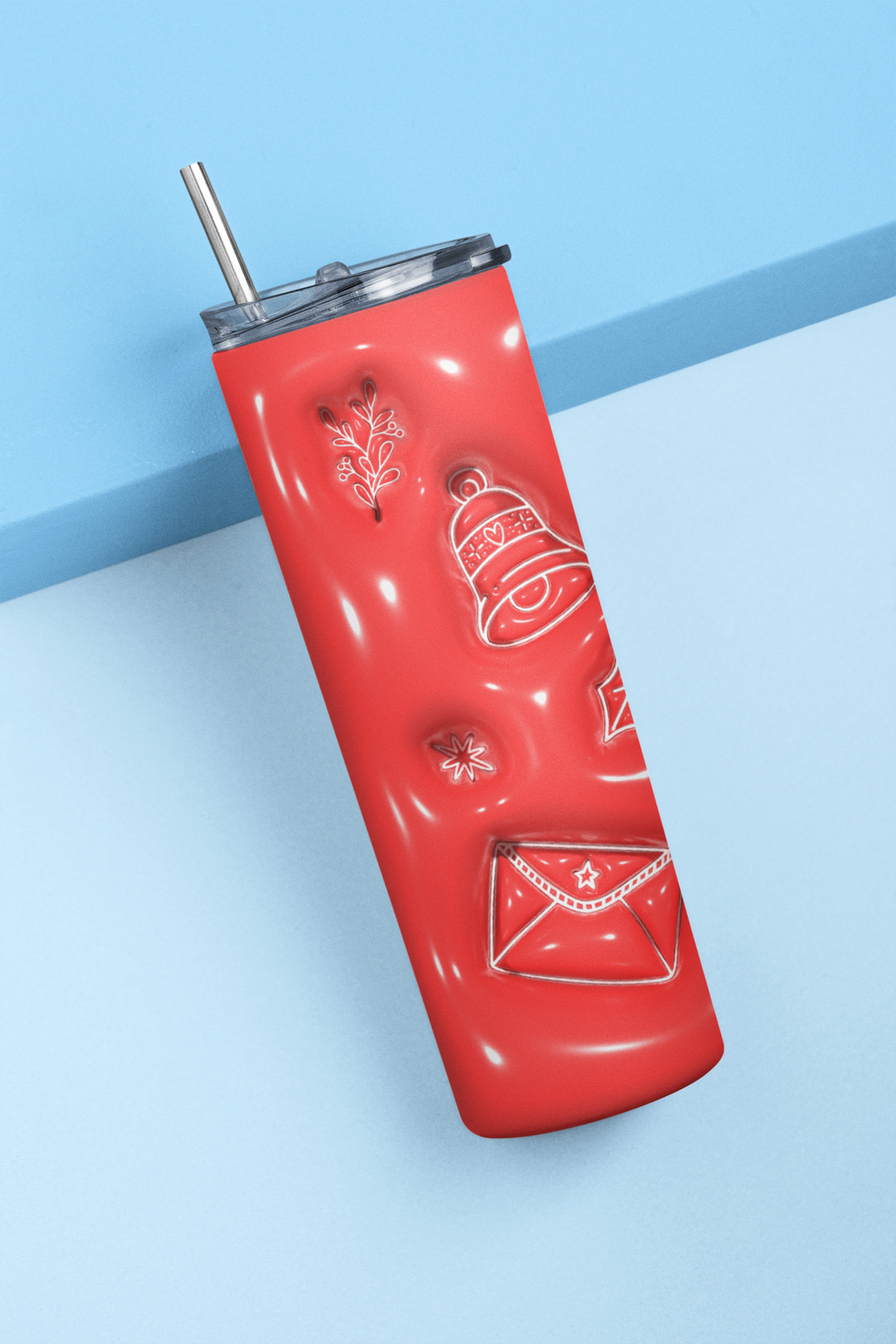 A glossy red insulated tumbler with a clear lid and metal straw, decorated with embossed holiday motifs including a bell, envelope, snowflake, and leaf, shown on a light blue background.