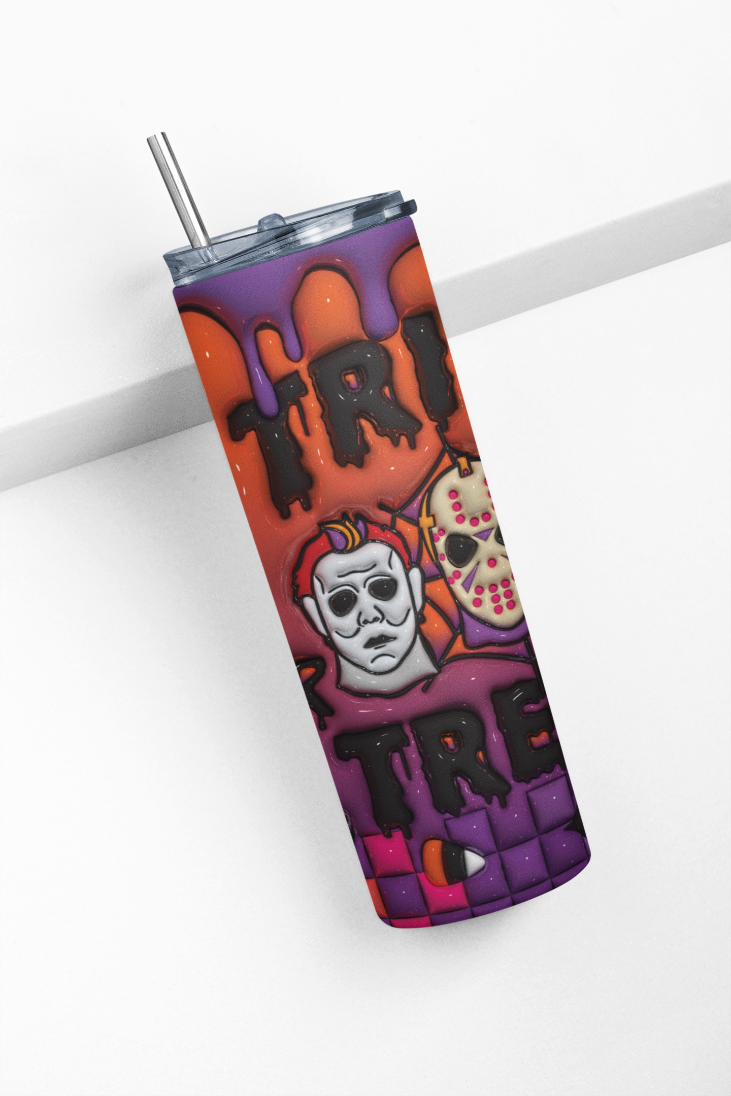 A tall insulated tumbler with a clear lid and metal straw, featuring a Halloween-themed graphic print with the word 'TREAT' in dripping black letters over orange and purple splatter shapes, plus a white skull illustration, shown on a clean white background.