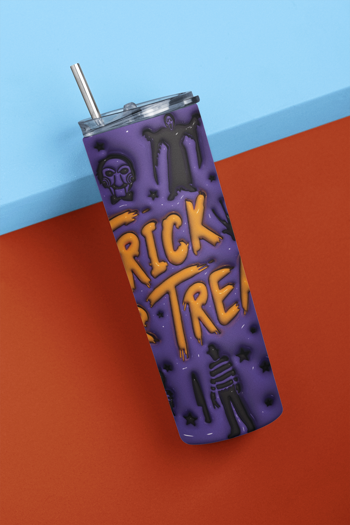 A purple Halloween-themed tumbler with a clear lid and metal straw, featuring raised black silhouettes and yellow 'Trick or Treat' lettering, photographed against a split blue and orange background.