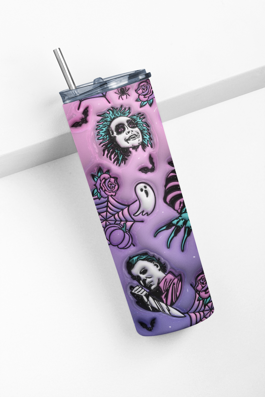 A tall insulated tumbler with a clear lid and metal straw, featuring a Halloween-style print with a purple-to-pink gradient, skulls, ghosts, spiders, roses, and bats.