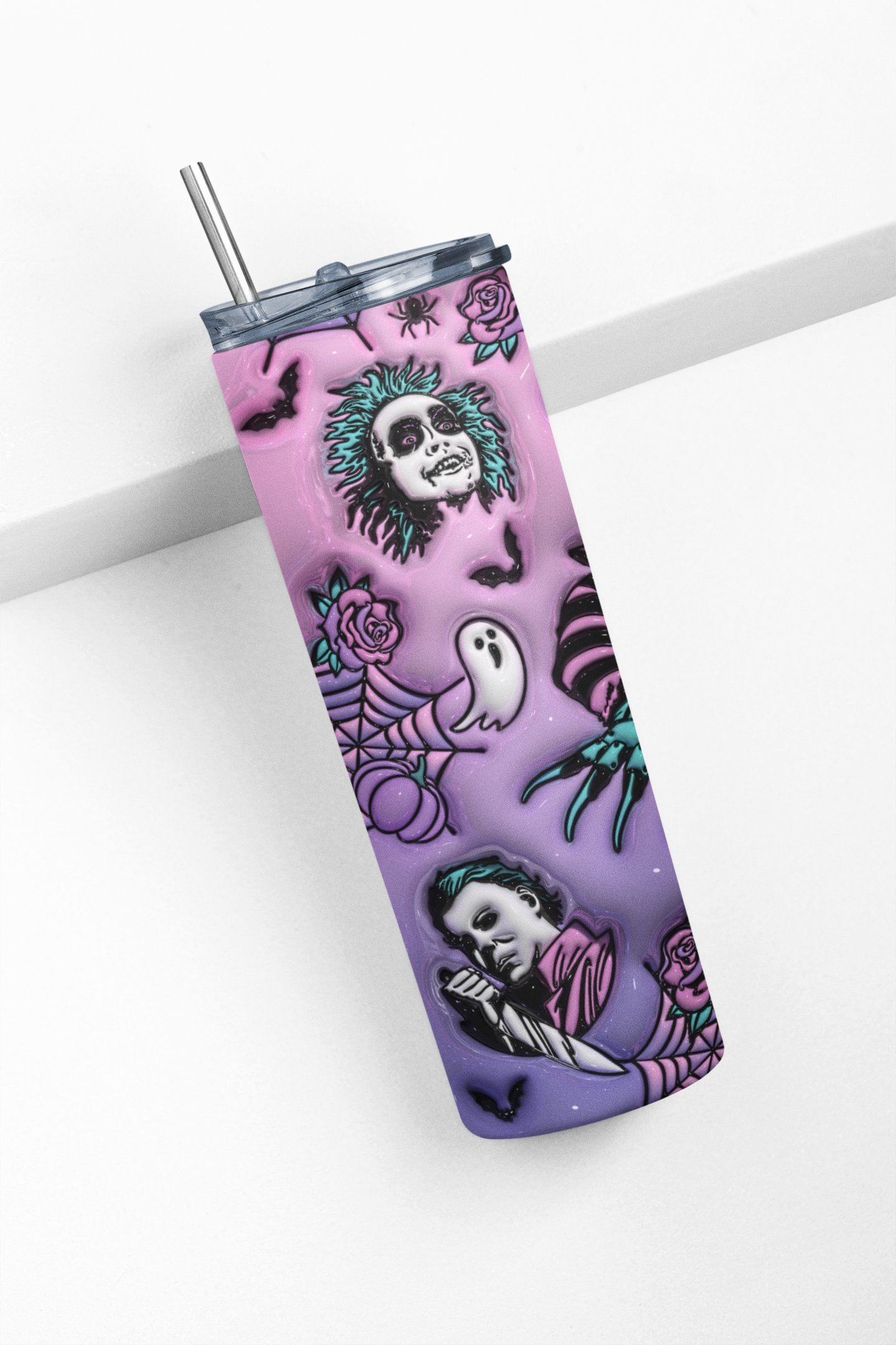 A tall insulated tumbler with a clear lid and metal straw, featuring a Halloween-style print with a purple-to-pink gradient, skulls, ghosts, spiders, roses, and bats.