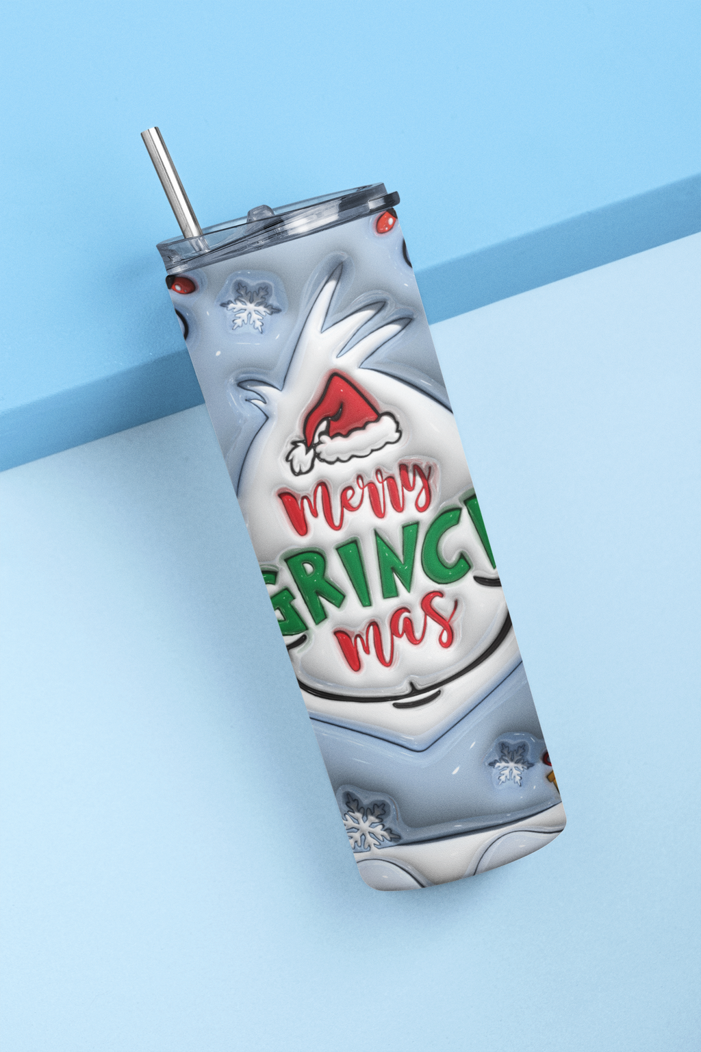 A stainless steel tumbler with a clear lid and metal straw, featuring a festive holiday design of a white reindeer wearing a Santa hat and the text 'Merry GRINCH mas' in red and green lettering, set against a light blue background.
