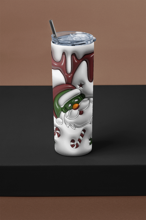 A tall insulated tumbler with a clear lid and metal straw, featuring a stylized Santa Claus face and holiday graphics in white, red, green, and black, displayed on a black platform against a brown background.