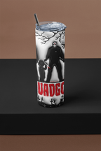 A tall insulated tumbler with a clear lid and black straw, featuring a black-and-white horror character illustration and bold red text reading 'UADGO' on a dark display surface against a brown backdrop.