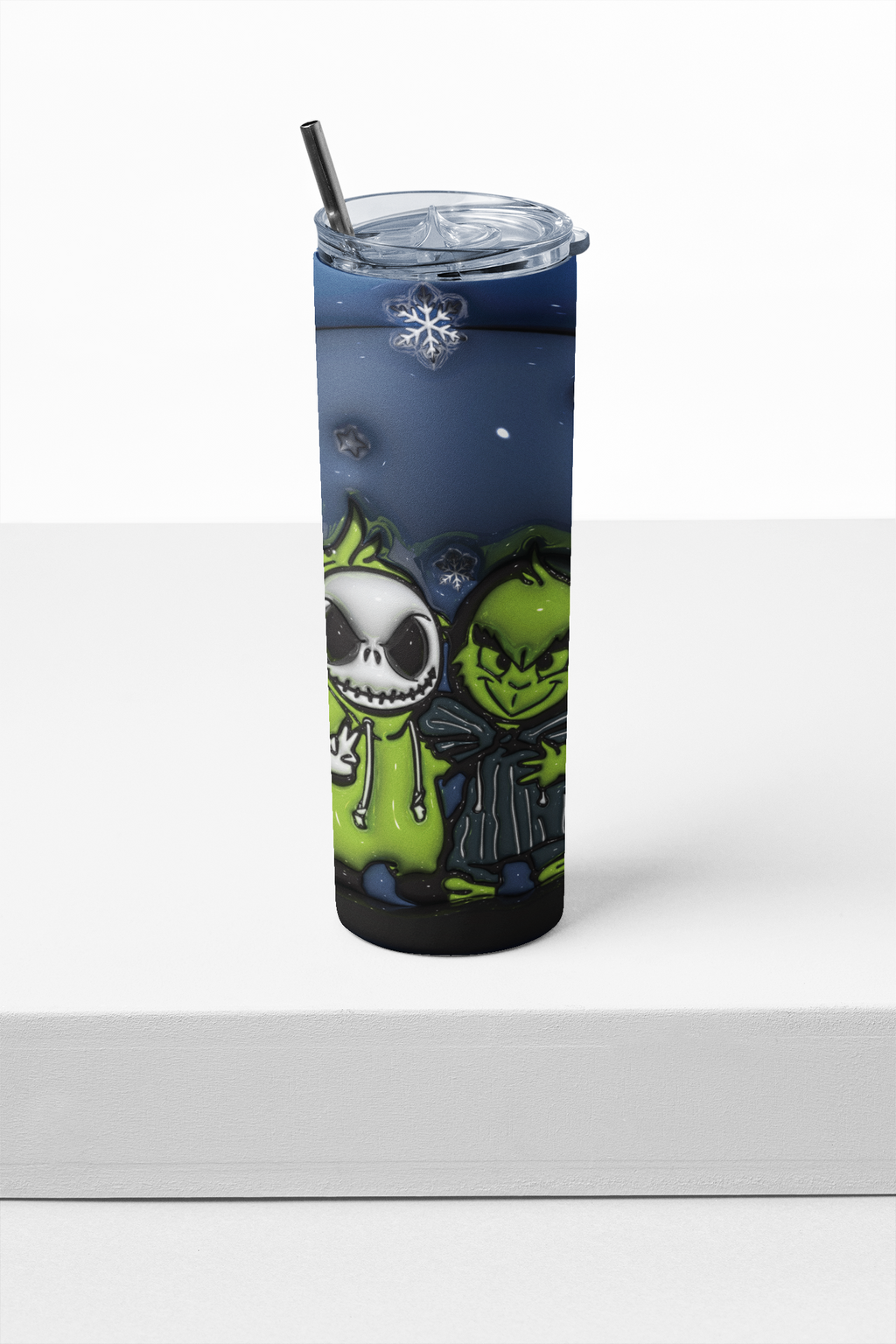 A tall insulated tumbler with a clear lid and black straw, featuring a printed design of Jack Skellington and the Grinch in green and black tones against a dark blue night sky, displayed on a white surface.