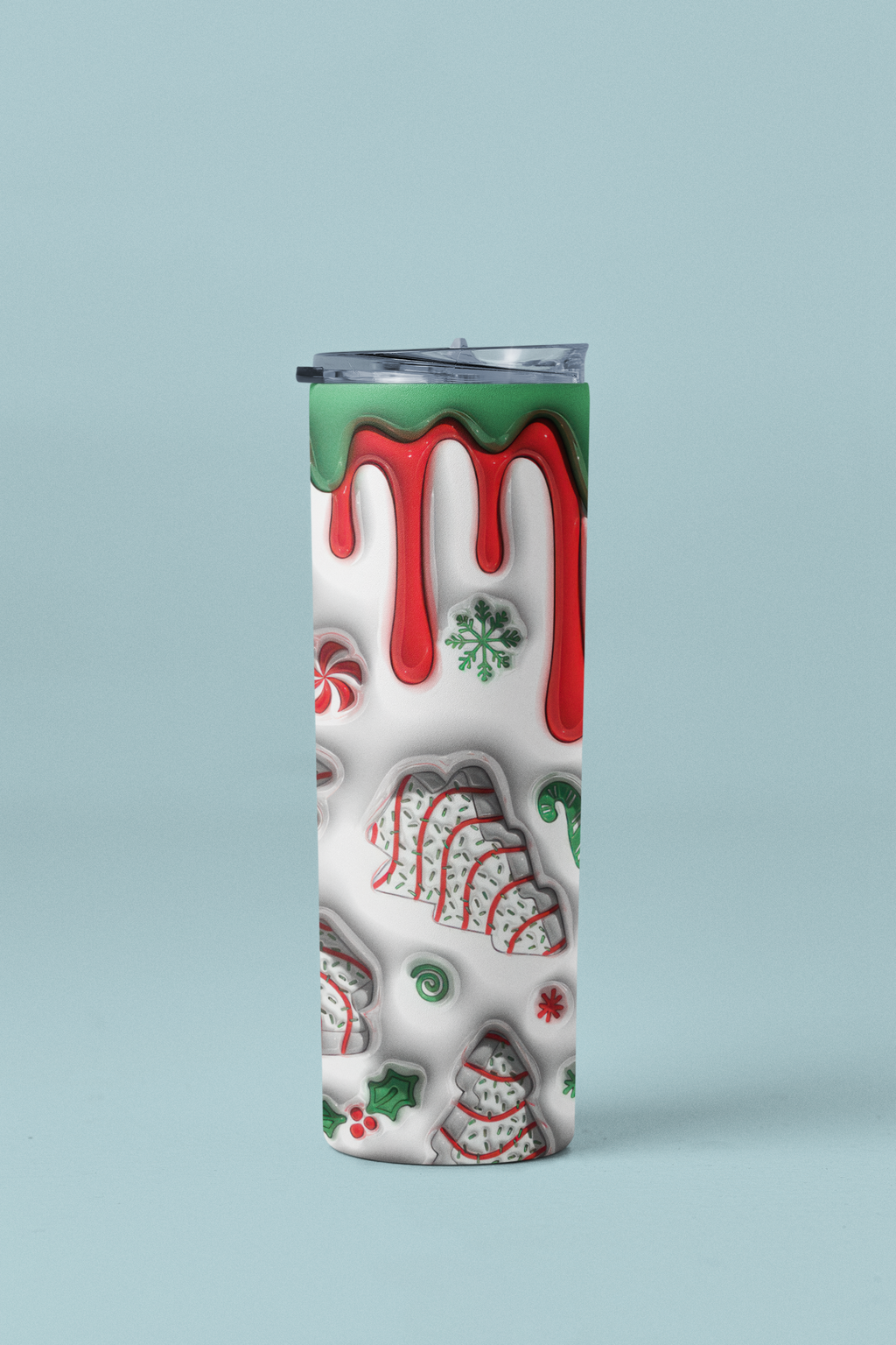 A tall, slim insulated tumbler with a clear lid, featuring a festive Christmas cookie and candy design on a white background with red dripping icing and green accents, set against a solid light blue background.