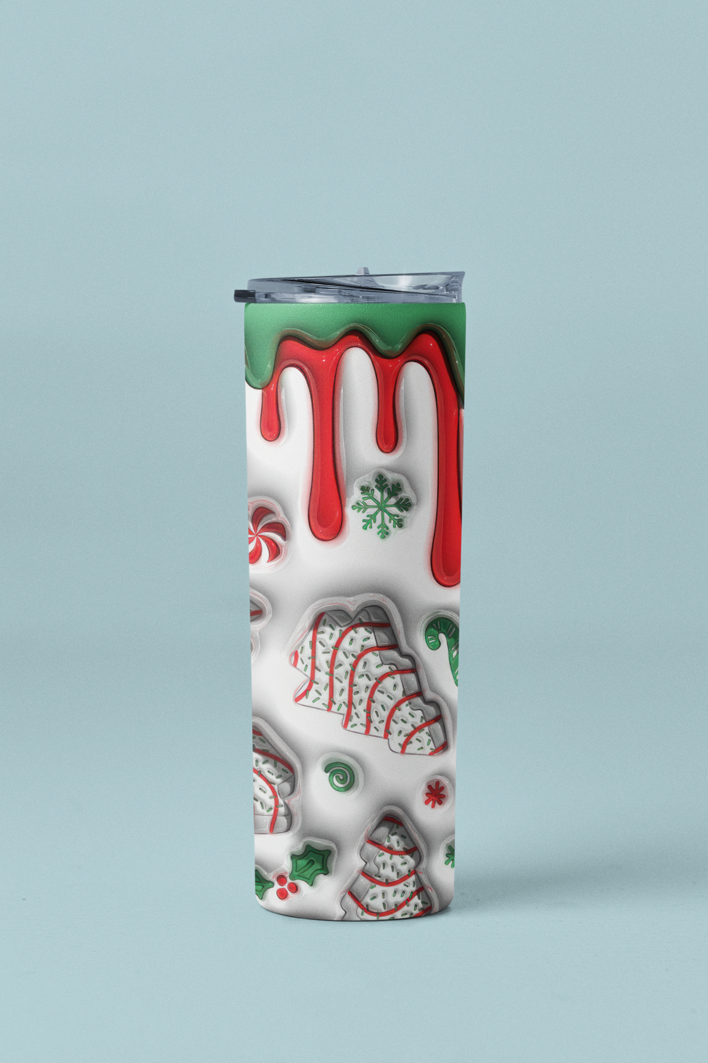A tall, slim insulated tumbler with a clear lid, featuring a festive Christmas cookie and candy design on a white background with red dripping icing and green accents, set against a solid light blue background.