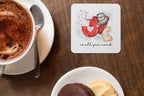 Cup of coffee with a coaster featuring a heart and owl illustration on a wooden table.