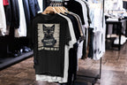 Black t-shirt with a graphic design of a cat and text on a rack in a store.