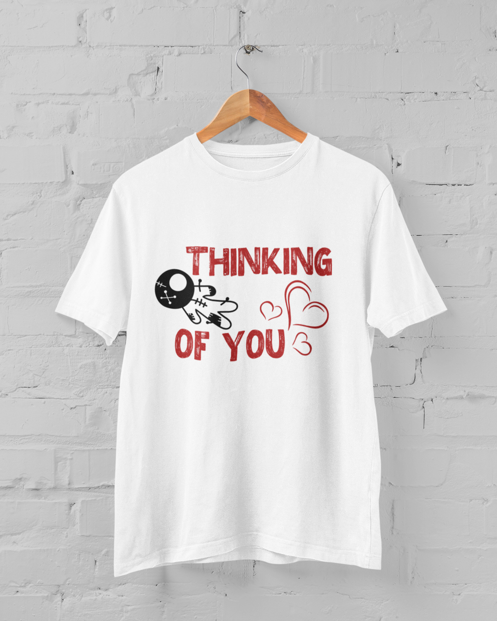 White t-shirt with red text and graphics on a hanger against a gray brick wall.
