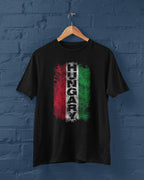 Black t-shirt with Hungarian flag design on a wooden hanger against a blue brick wall.