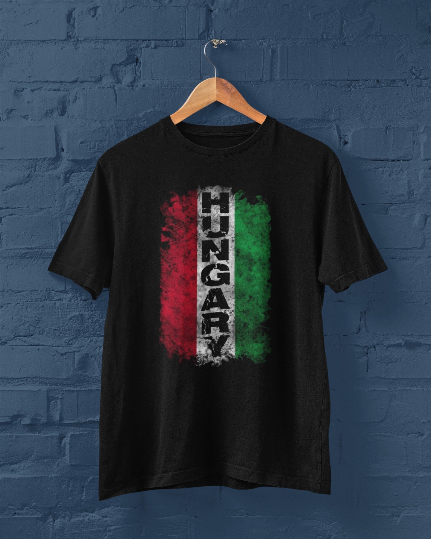 Black t-shirt with Hungarian flag design on a wooden hanger against a blue brick wall.