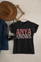 Black t-shirt with 'ANYA KNOWS' text, hat, denim jacket, and camera on a neutral background