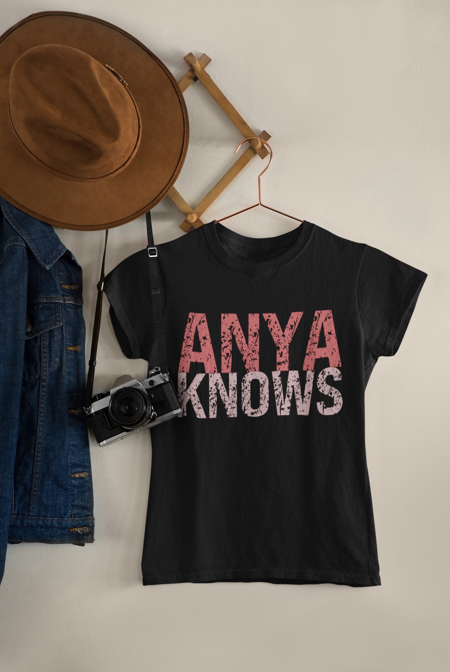 Black t-shirt with 'ANYA KNOWS' text, hat, denim jacket, and camera on a neutral background
