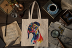 A canvas tote bag with a colorful watercolor-style dog portrait, displayed in a styled flat-lay on a dark wooden table surrounded by vintage books, a cup of coffee, a magnifying glass, and other antique props.