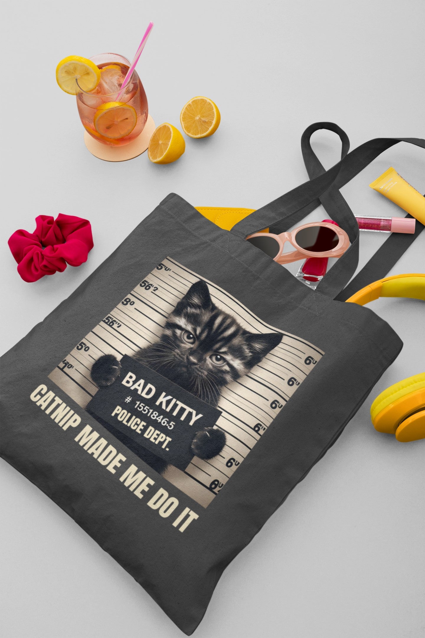 Tote bag with a cat graphic and text on a table with a drink and snacks.