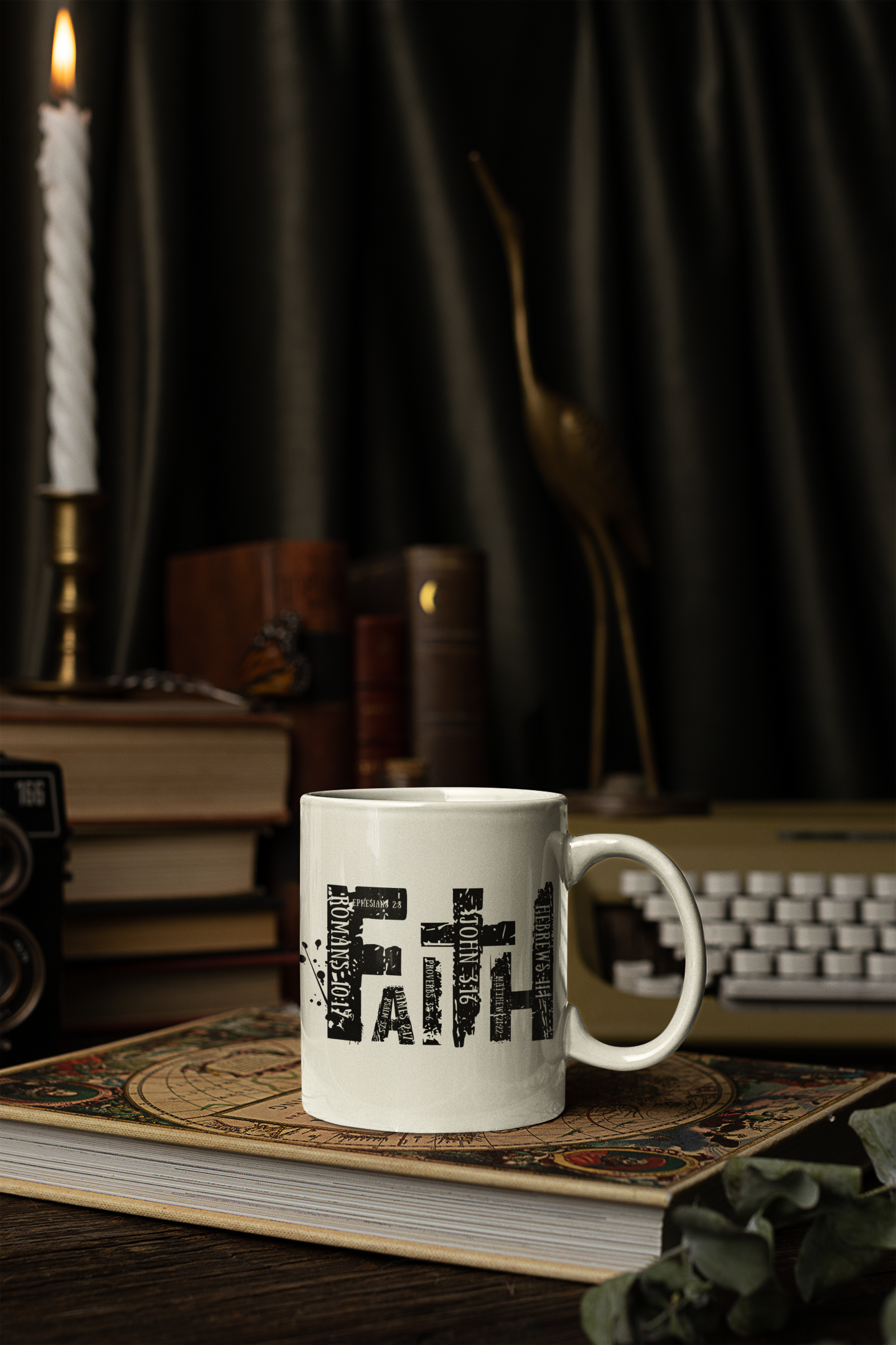 A white ceramic coffee mug with the word 'Faith' printed in a black distressed typographic font, resting on a vintage book. The background is a dark, moody setting with a burning candle, old books, a brass bird sculpture, and a retro computer keyboard.