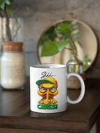 A white ceramic coffee mug with a cartoon owl graphic sitting on a dark wooden table. The graphic shows a yellow owl wearing a green cap and glasses with the text 'Shhh.