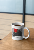 A white ceramic coffee mug filled with black coffee sits on a wooden table in a modern indoor setting with a blurred window background. The mug features a graphic print of a person wearing a red hoodie and the text 'DREAM BIG, STAY WONE' and 'KEEP FIGHTING'.