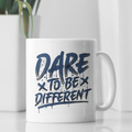 A white ceramic mug with the text 'DARE TO BE DIFFERENT' printed in dark navy blue, set on a reflective white surface with a blurred white plant in the background.