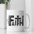 A white ceramic coffee mug with a black typographic design spelling 'FAITH' using words from the Bible, set on a white surface with a blurred white plant in the background.