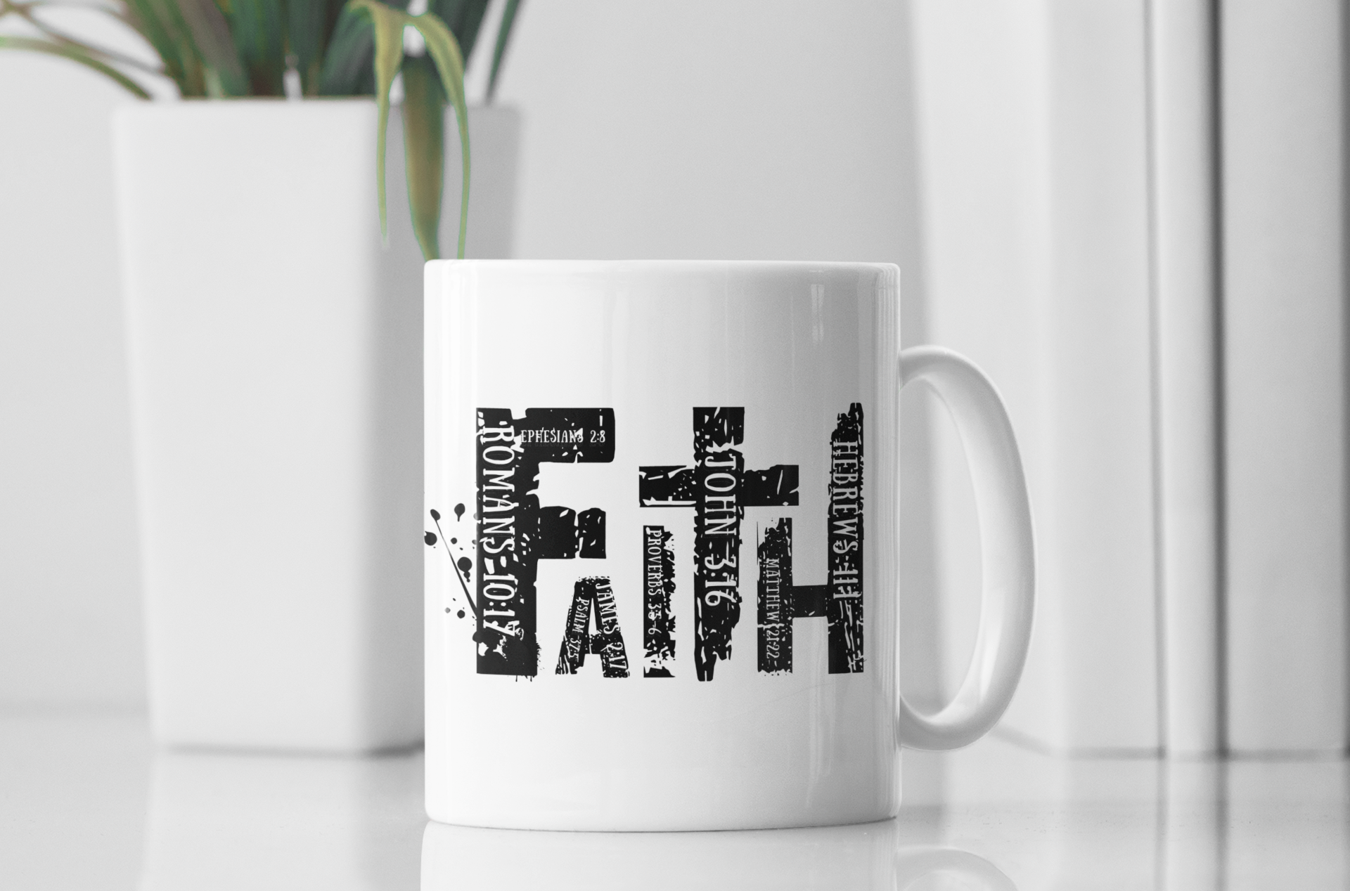 A white ceramic coffee mug with a black typographic design spelling 'FAITH' using words from the Bible, set on a white surface with a blurred white plant in the background.