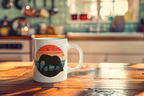 A white ceramic mug with a retro sunset and elephant graphic sits on a wooden table in a warm, blurred kitchen setting.