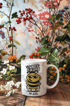 A white ceramic coffee mug with a cartoon bee graphic and the text 'WHY THE BEE CAUSE I'M COOL' sits on a wooden table surrounded by decorative flowers and berries.