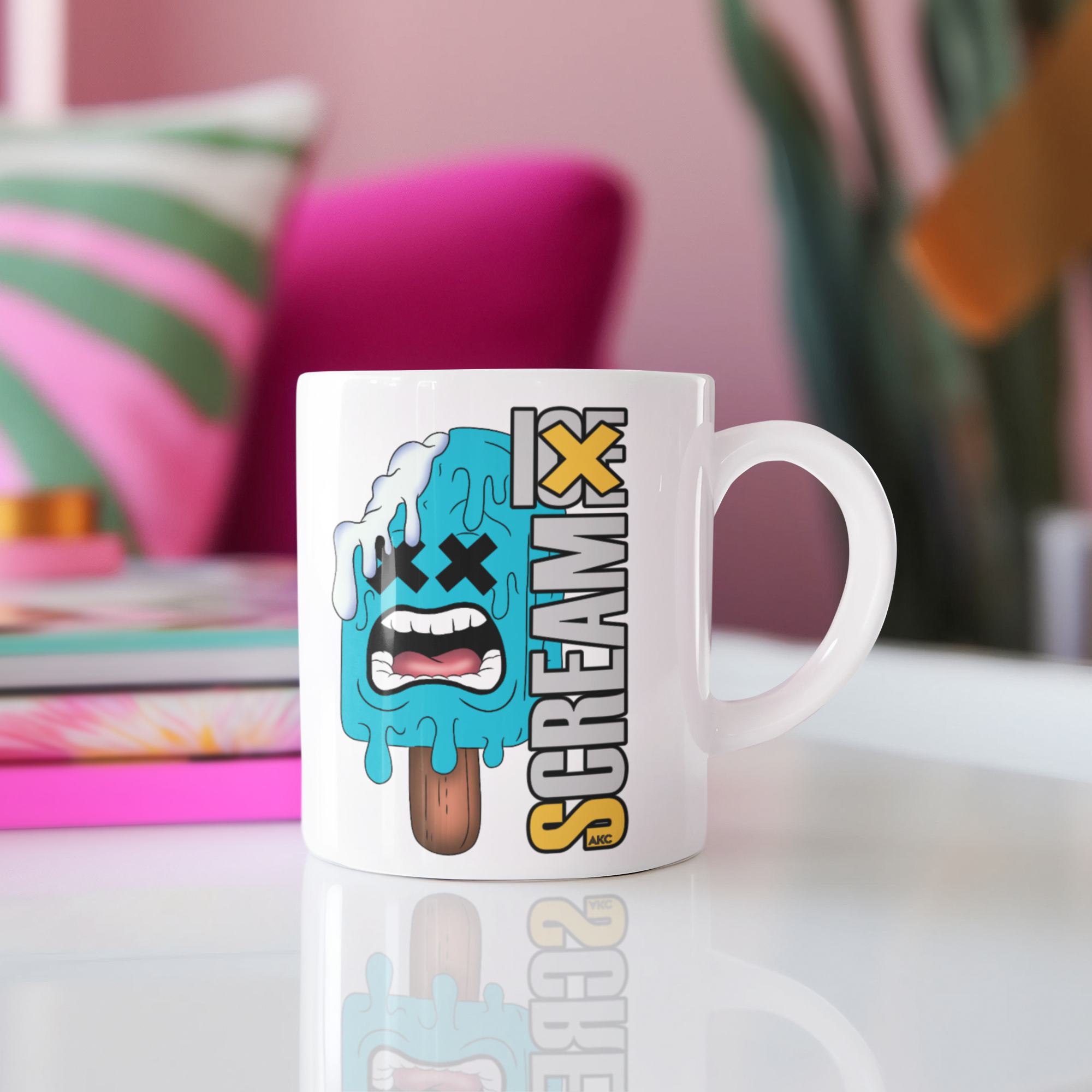A white ceramic coffee mug with a cartoon graphic of a melting blue popsicle and the word 'SCREAM FX' in yellow, black, and white, set on a white reflective table with a blurred pink background.