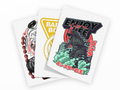 Three overlapping white art prints or stickers on a light gray background. The front print shows a dark monster standing in green smoke with large black, red, and white text reading 'ENJOY LIFE' and Japanese characters.