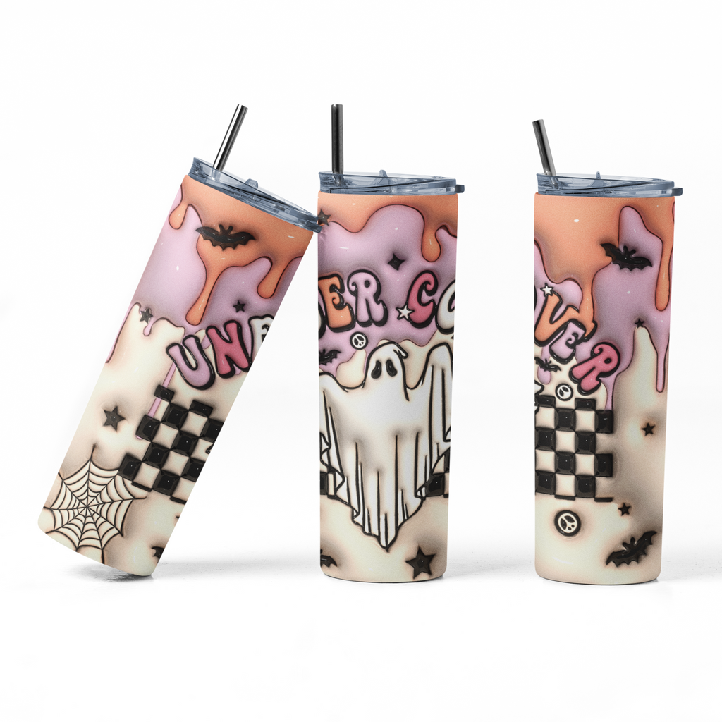 Three views of a Halloween-themed skinny tumbler with a clear lid and black straw. The design features dripping pink frosting, a ghost, a spiderweb, a black-and-white checkerboard pattern, and the words 'UNBEZIER' and 'EVER COLDER'.