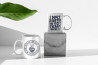 Two white ceramic mugs with black printed text and a hand gesture design, styled on a white surface with a concrete block and a green leaf in the background.