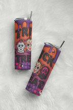 Two slim stainless steel tumblers with clear lids and metal straws, decorated with a Halloween-themed orange-to-purple gradient design featuring skulls, ghosts, and the word 'TREAT', photographed on a white faux-fur surface.