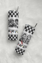 Two slim stainless steel tumblers with clear lids and metal straws, featuring a black and white checkerboard pattern, a black and white graphic of three characters, and the 'Friends' logo, displayed on a white faux fur background.