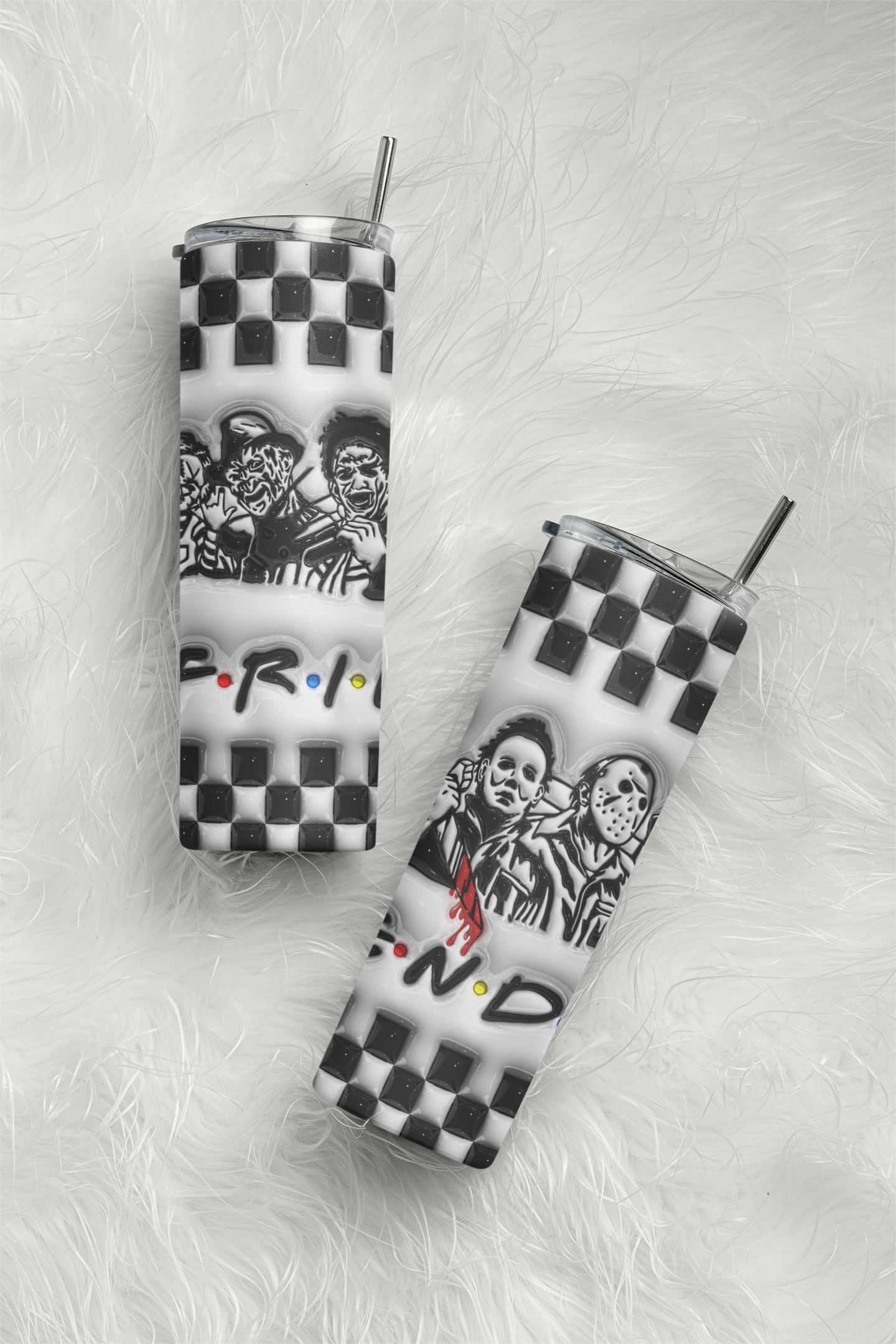 Two slim stainless steel tumblers with clear lids and metal straws, featuring a black and white checkerboard pattern, a black and white graphic of three characters, and the 'Friends' logo, displayed on a white faux fur background.