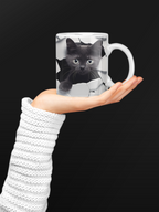 Mug with a black cat design held in a hand against a black background