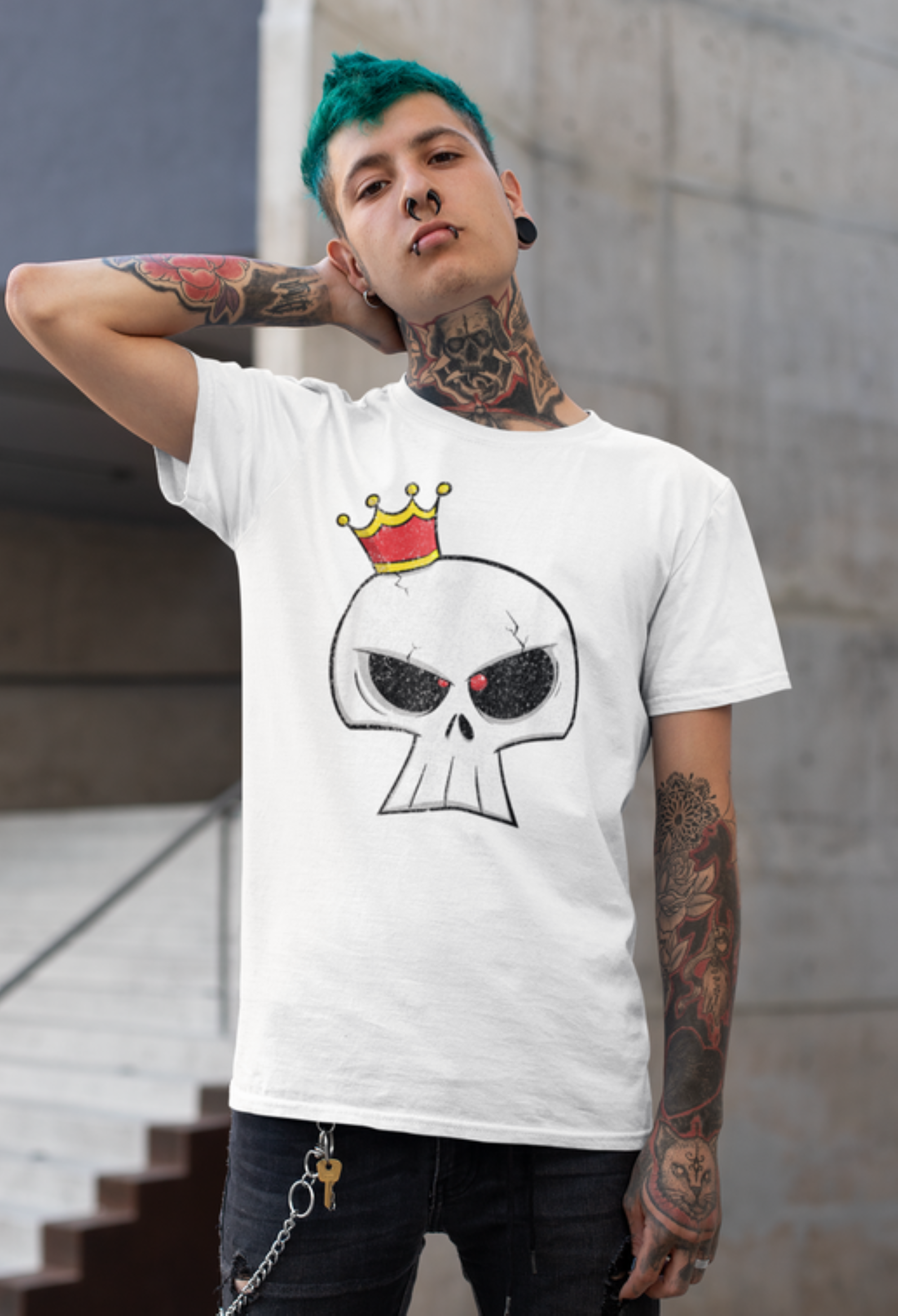 Person wearing a white t-shirt with a skull design and red crown, standing against a concrete wall.