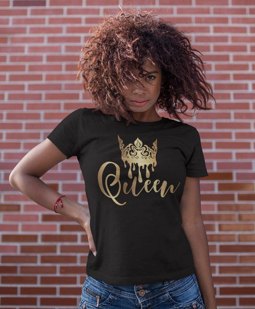 Woman wearing a black t-shirt with 'Queen' printed in gold against a brick wall.
