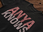 Black t-shirt with pink and white text on a wooden surface