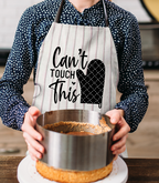 Person wearing an apron with 'Can't Touch This' text and an oven mitt graphic, holding a metal container.