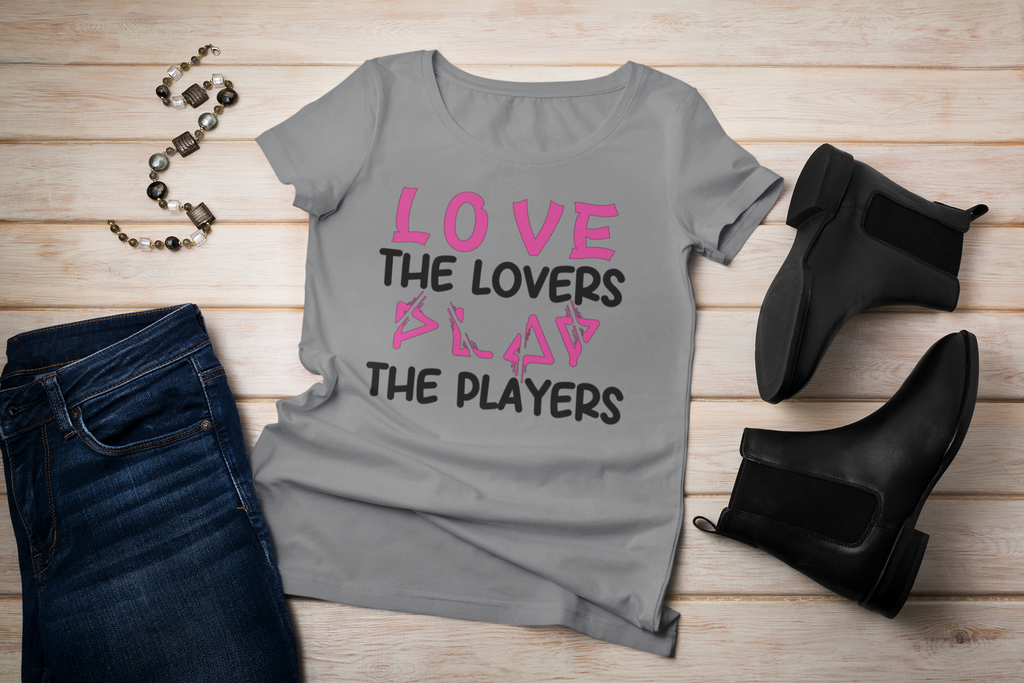 Gray t-shirt with 'LOVE THE LOVERS SLAY THE PLAYERS' text, paired with black jeans and boots on a wooden surface.