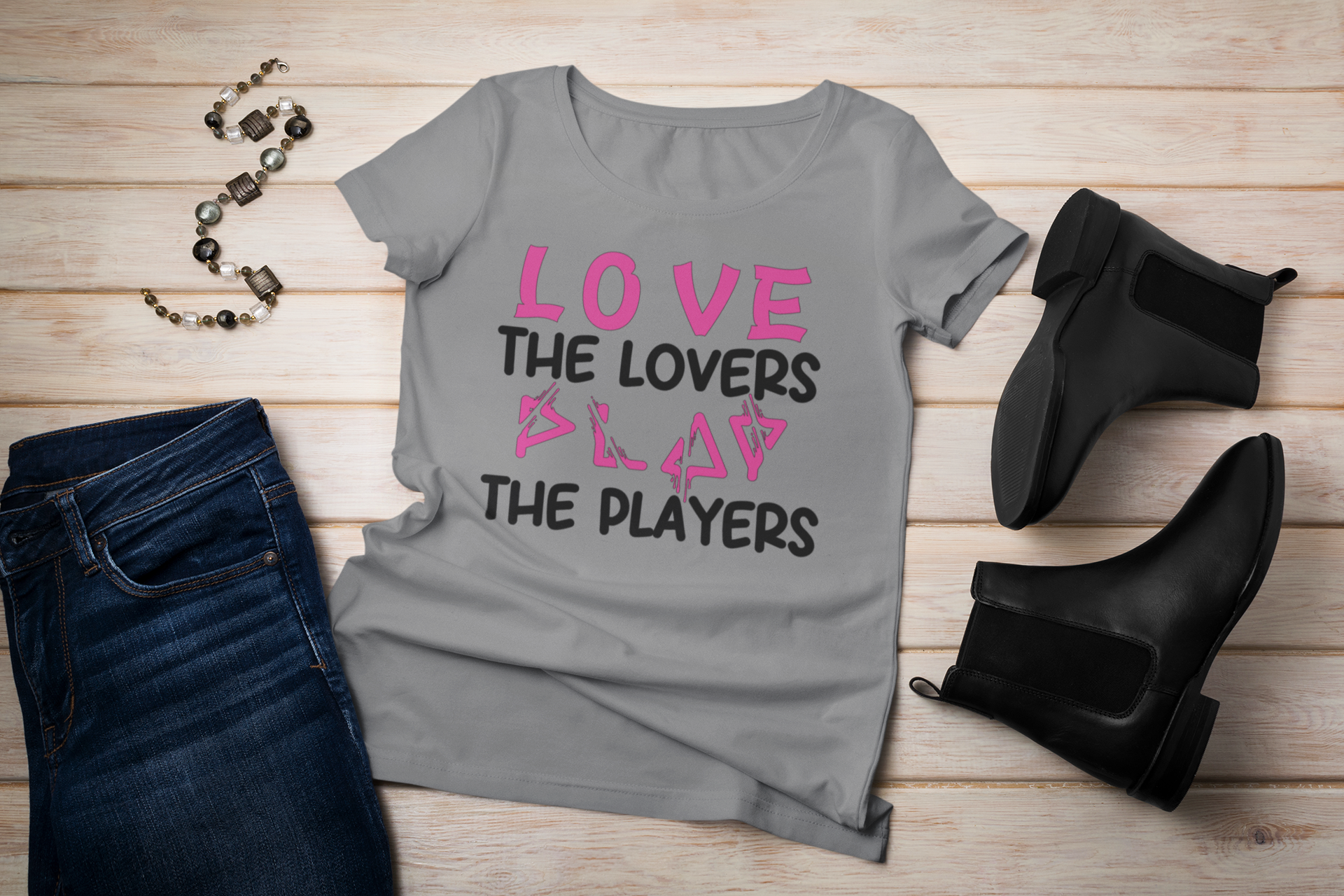 Gray t-shirt with 'LOVE THE LOVERS SLAY THE PLAYERS' text, paired with black jeans and boots on a wooden surface.