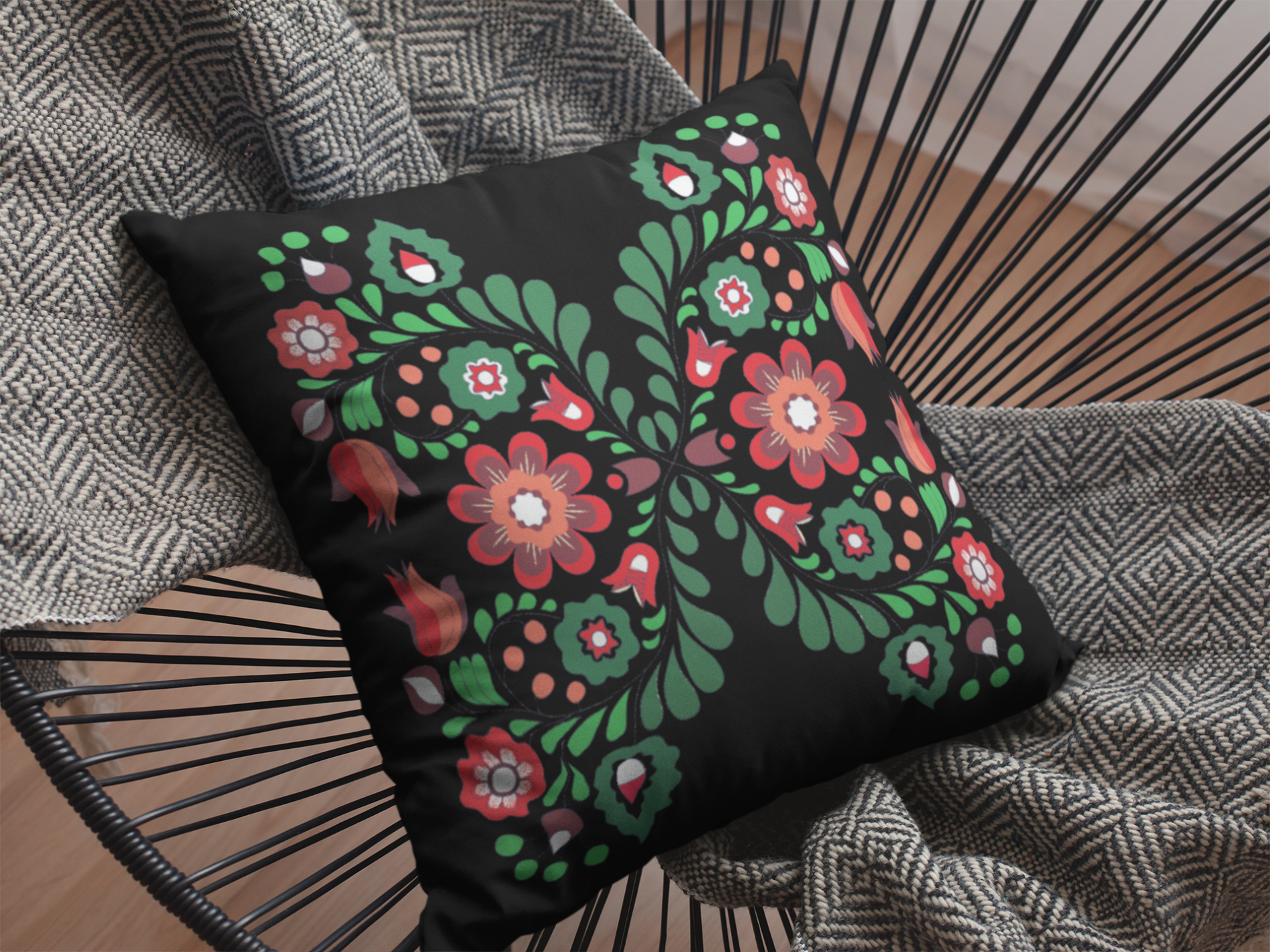 Decorative pillow with floral patterns on a black background, placed on a wicker chair.