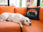 White dog lying on an orange couch next to a black pillow with a bear design.