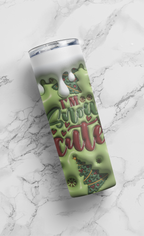 A tall insulated tumbler with a clear lid, featuring a green holiday design with dripping white liquid, red script text reading 'I'M Your cute', and a Christmas tree illustration, shown on a white marble surface.