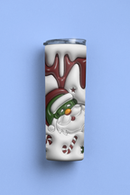 A slim stainless steel tumbler with a holiday design featuring a snowman wearing a Santa hat, candy canes, and white snow with dark red accents, set against a solid light blue background.