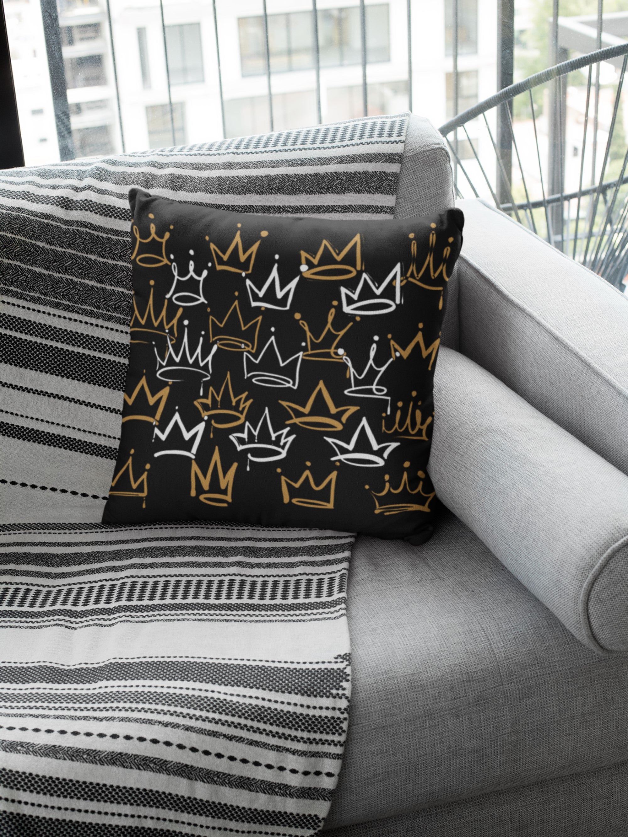 Decorative pillow with crown pattern on a gray sofa with striped blanket