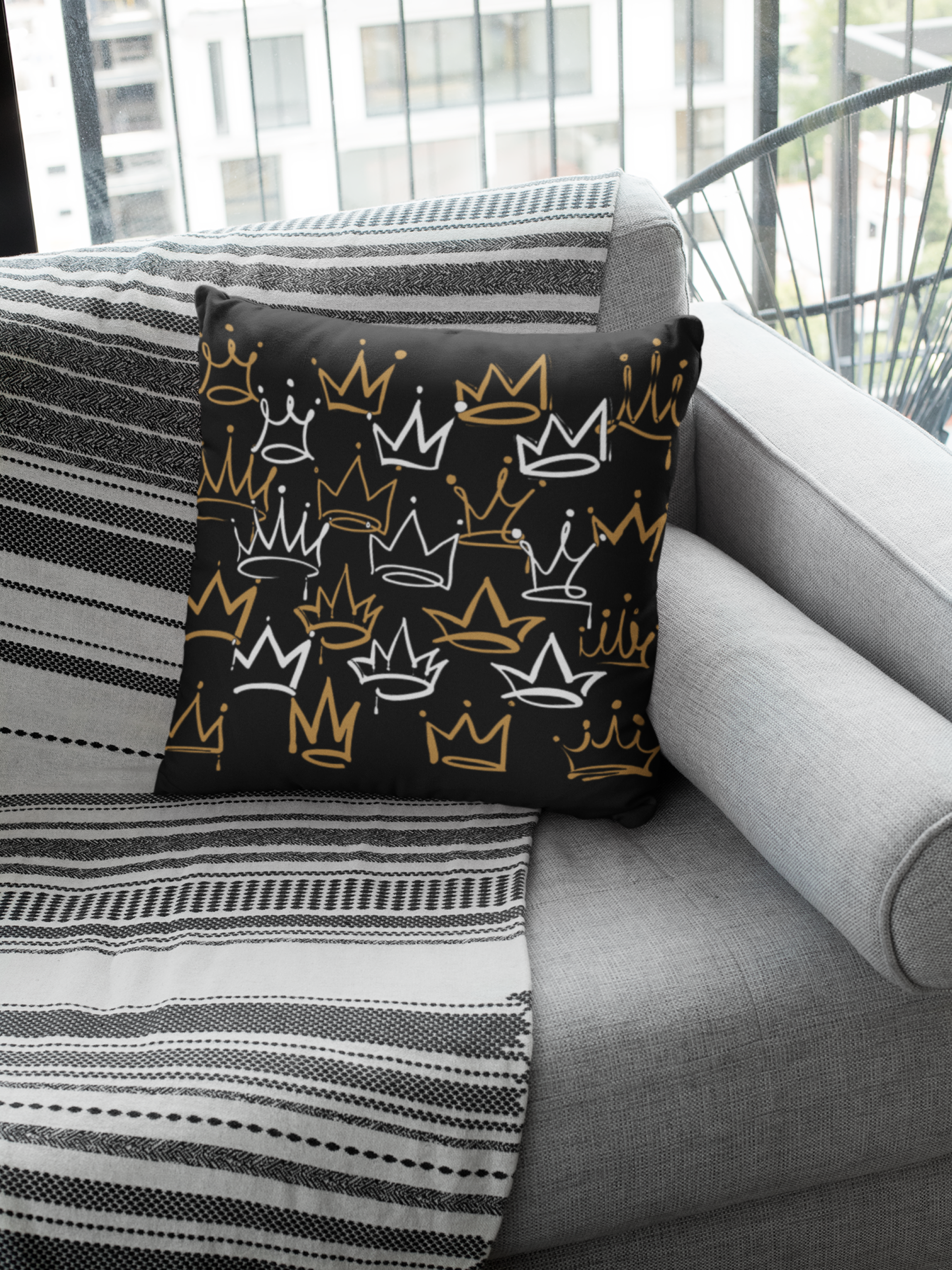 Decorative pillow with crown pattern on a gray sofa with striped blanket