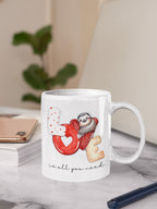 White mug with a design of a sloth, heart, and cookie on a marble surface.
