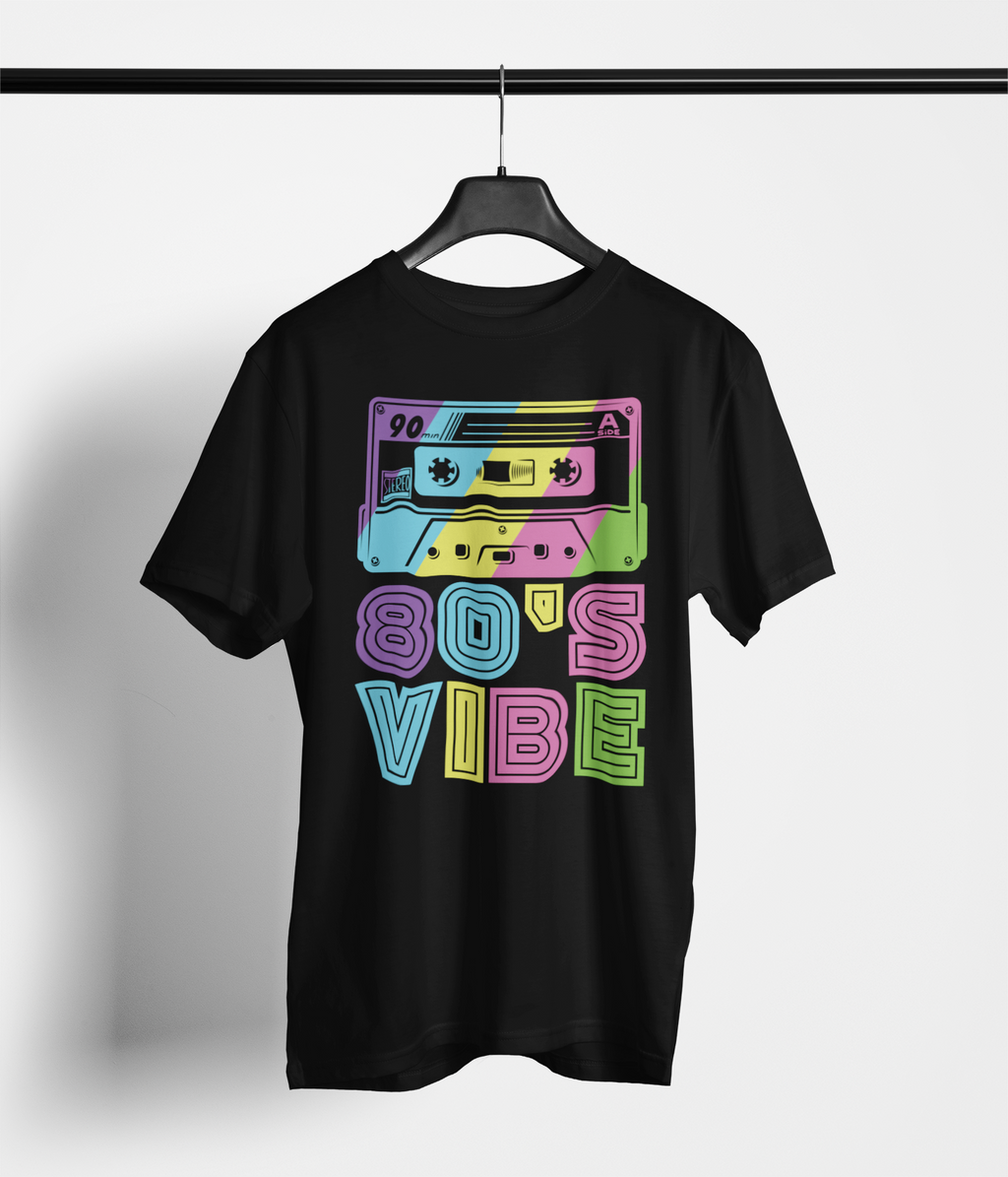 A black short-sleeve t-shirt hanging on a black hanger against a light gray wall. The shirt features a colorful retro graphic of two cassette tapes above the text '80'S VIBE' in a neon, multi-colored bubble font.